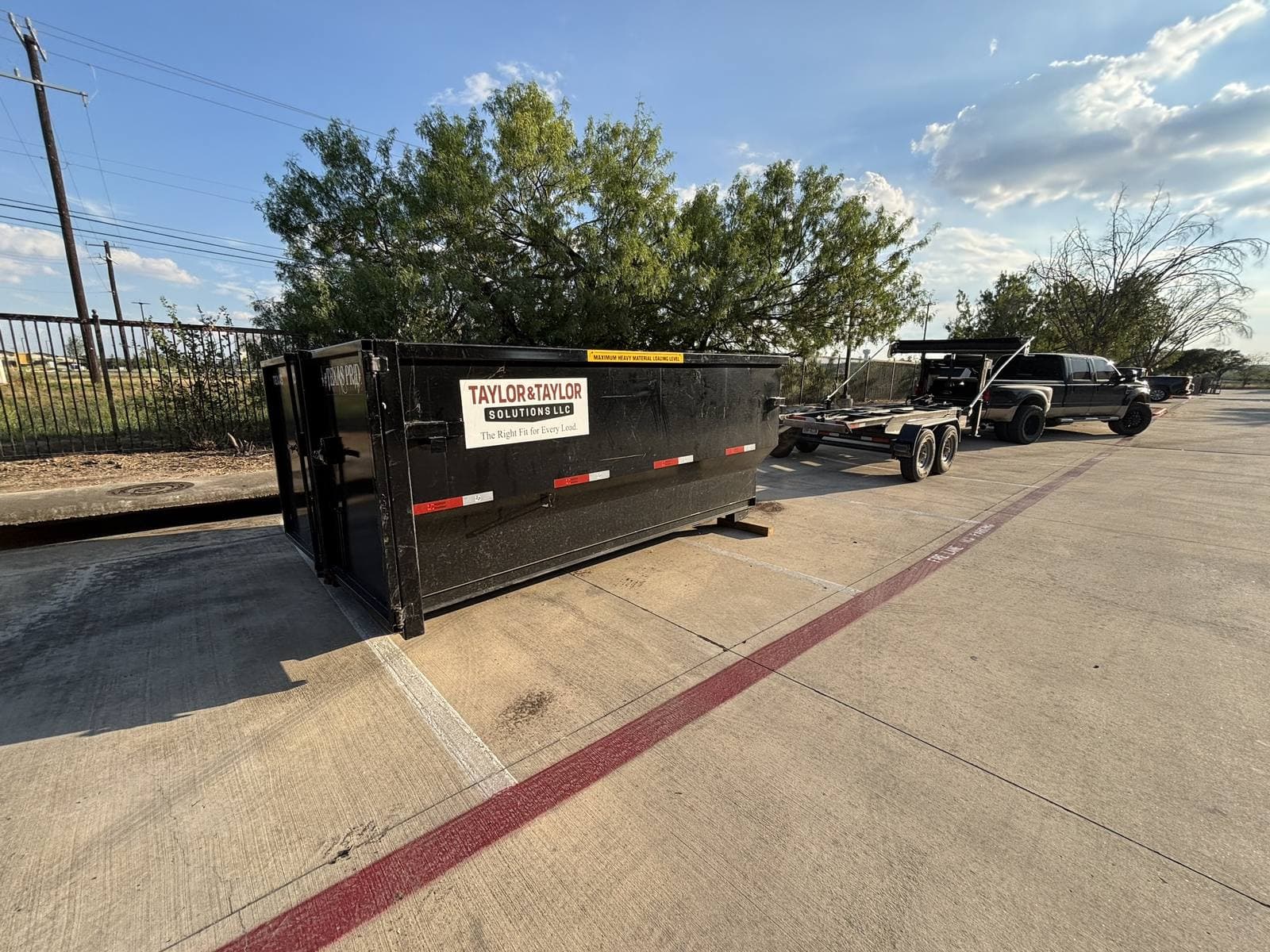 Branded Taylor & Taylor dumpster dropped in a commercial parking lot, truck and trailer behind