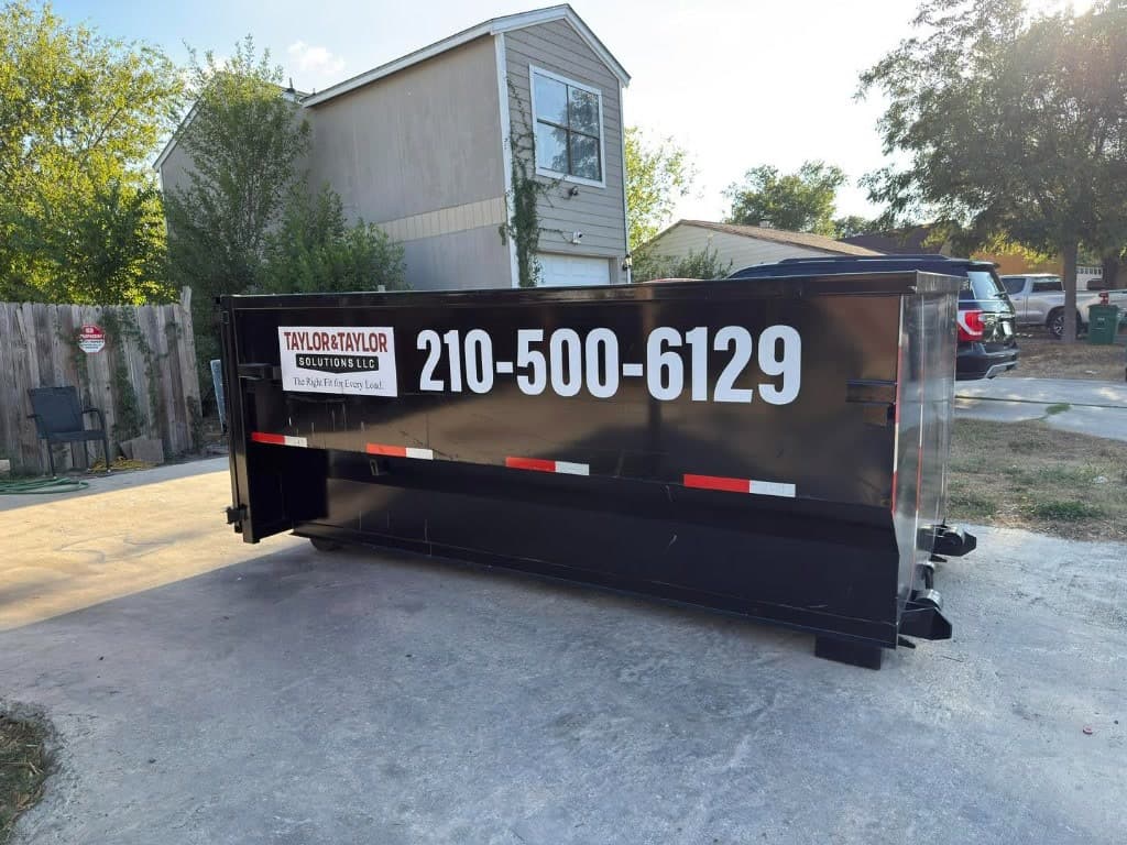 Black Taylor & Taylor dumpster on a residential driveway in front of a beige home